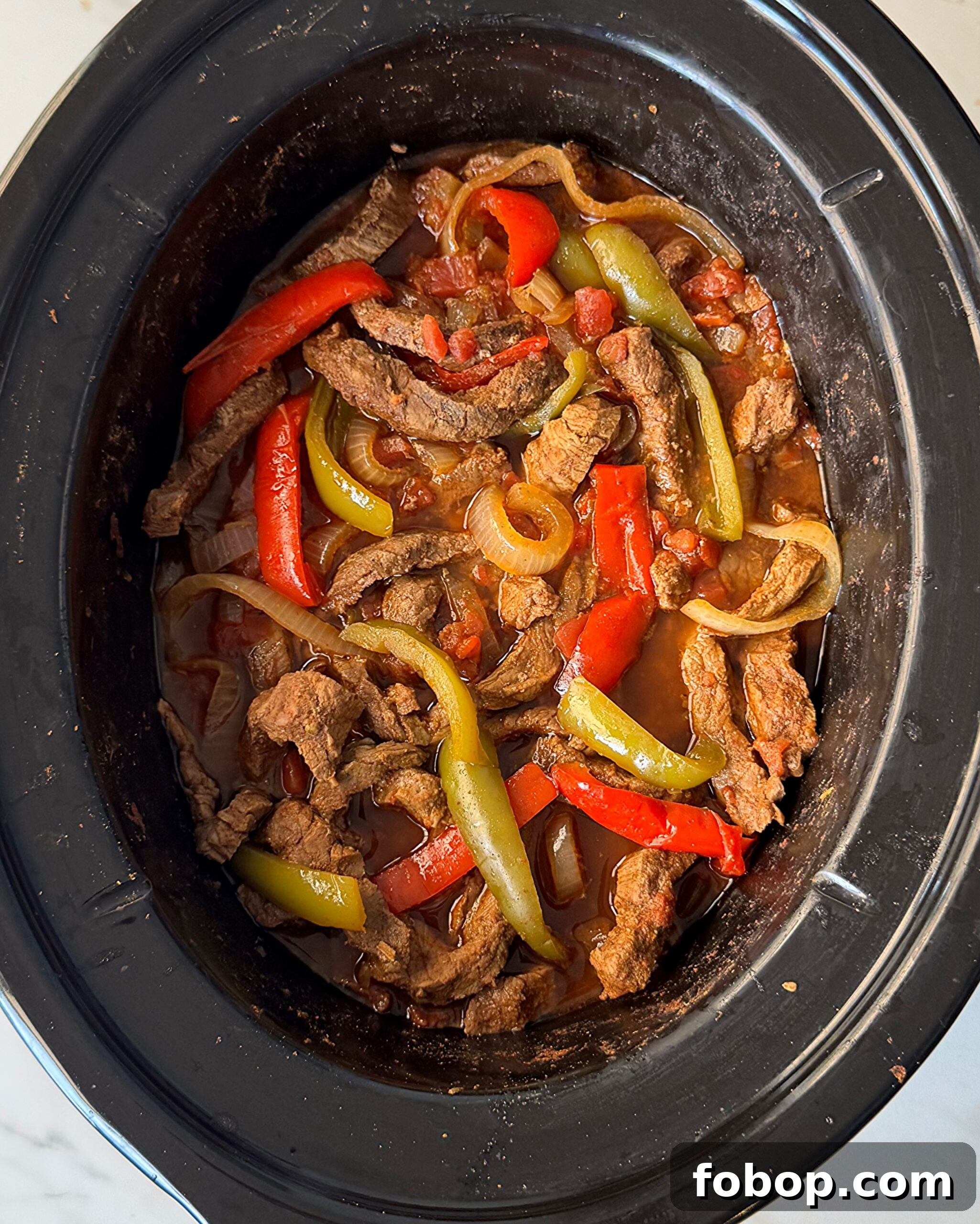 overhead shot of cooked steak fajitas in a black slow cooker