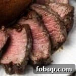 Close up of air fryer filet mignon cut into slices next to a baked potato on a plate.