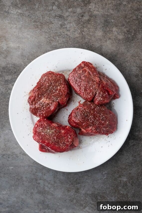 Four seasoned filet mignon steaks on a plate.