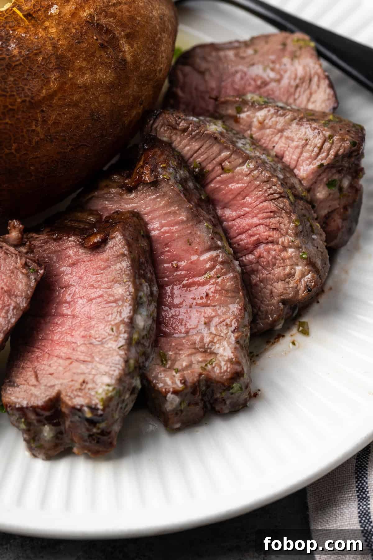 Close up of air fryer filet mignon cut into slices next to a baked potato on a plate.
