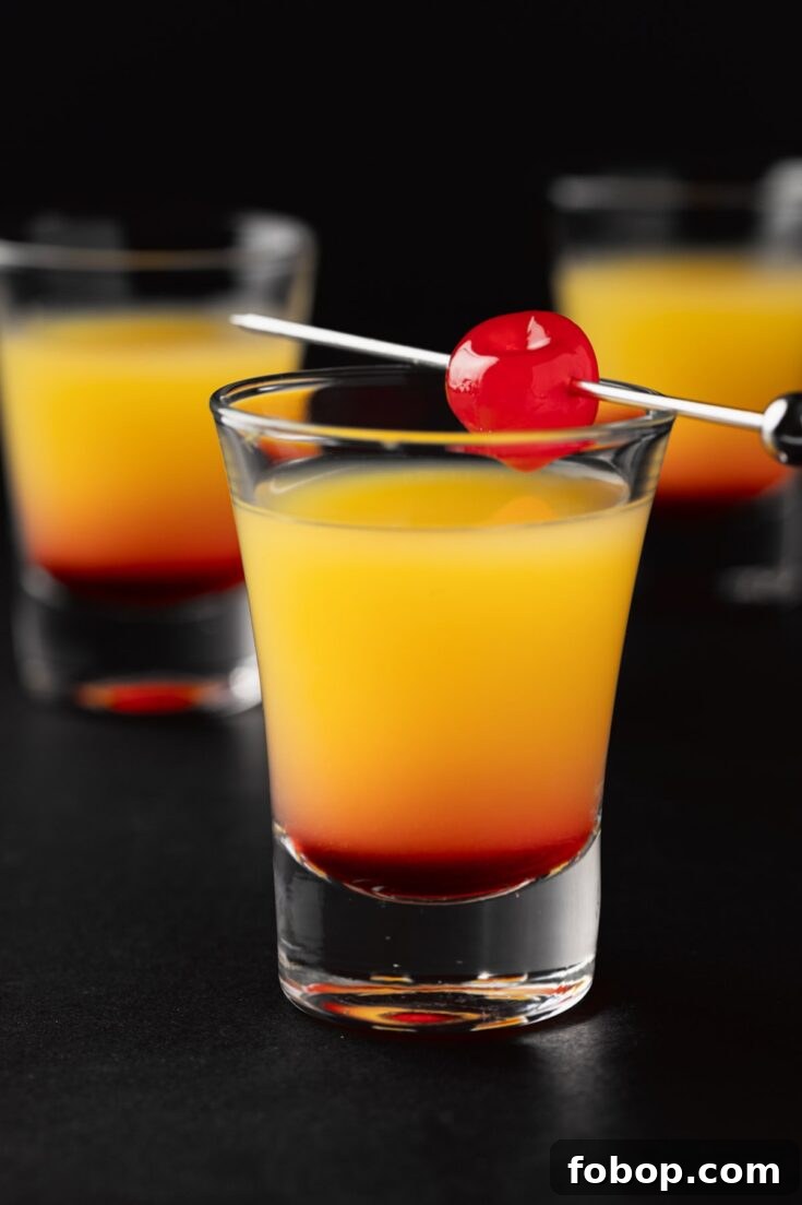 Three Tequila Sunrise Shots garnished with a maraschino cherry on a black background.