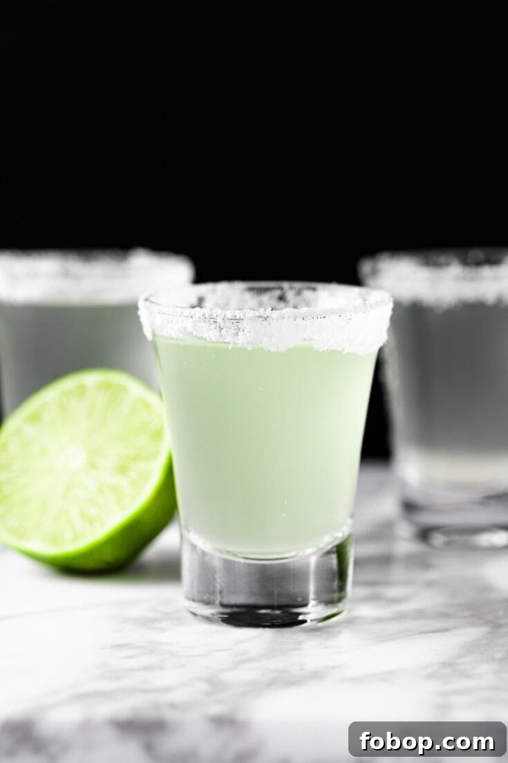 Three margarita shooters with a salted rim, next to half a lime.