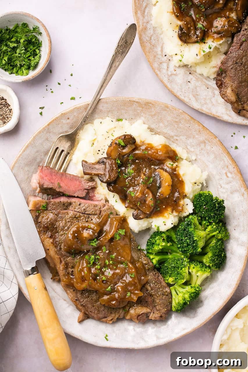 Instant Pot Steak in Rich Homemade Beef Gravy 2 Instant Pot steak served with homemade onion-mushroom gravy, mashed potatoes, and broccoli on a plate with a fork and a steak knife