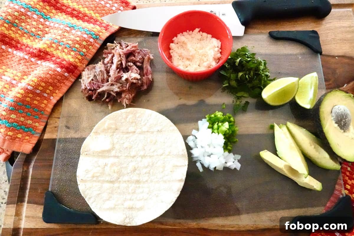 Smoked Pulled Pork Tacos with Tangy Pineapple Slaw 3 ingredients for pulled pork tacos on cutting board: smoked pork, cotija cheese, cilantro, lime, avocado, onion, jalapeño, and corn tortilla