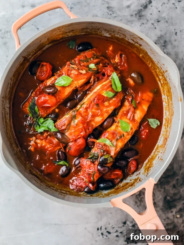 Sauté pan with salmon fillets in tomato and red wine sauce garnished with fresh basil.