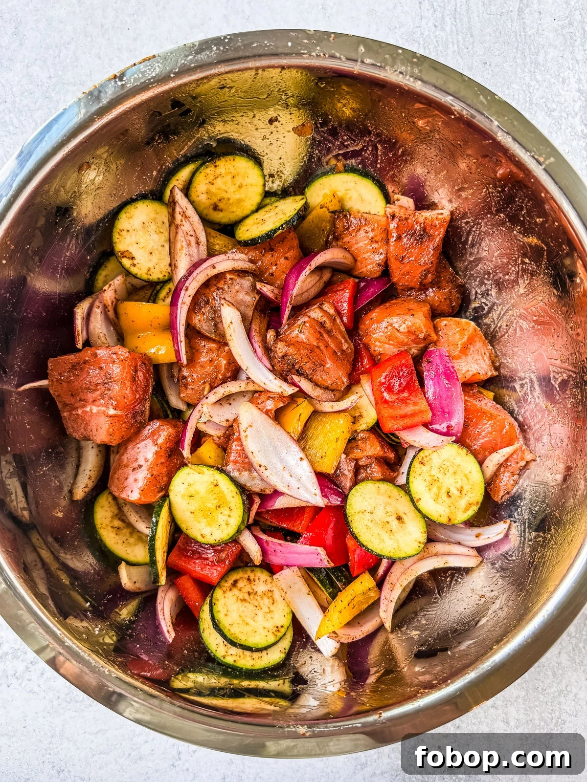 Salmon and vegetables tossed in marinade in a large mixing bowl.