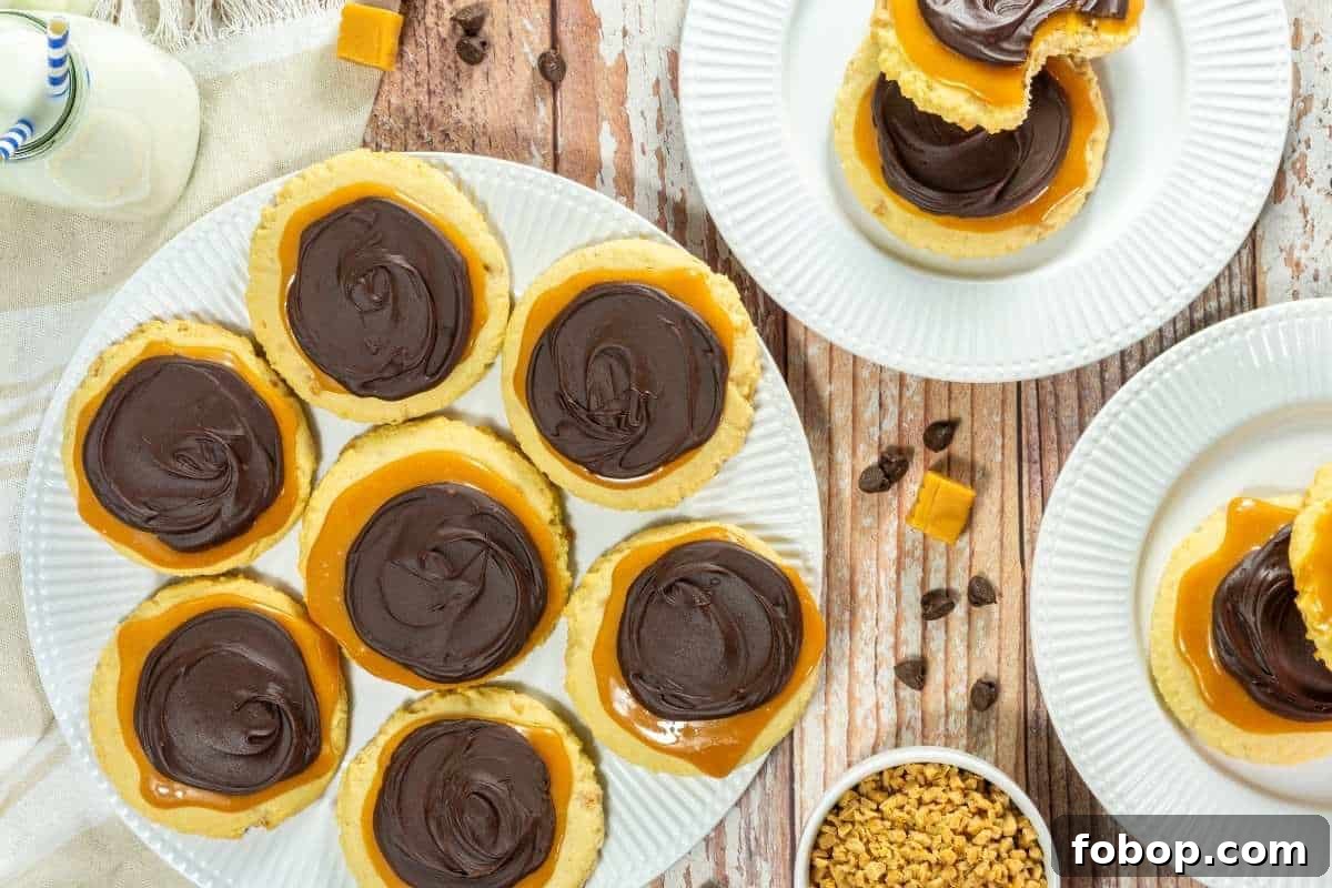 25 Office Cookies Everyone Brings and Raves About 17 A plate of Copycat Crumbl Twix Cookies, with more cookies on separate plates, caramel pieces, and small chocolate chips nearby on a wooden table.