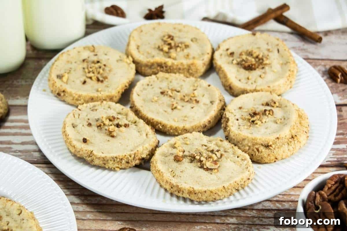 25 Office Cookies Everyone Brings and Raves About 19 A white plate holds eight round Pecan Shortbread Cookies topped with chopped nuts, placed on a wooden surface next to bottles of milk and cinnamon sticks.