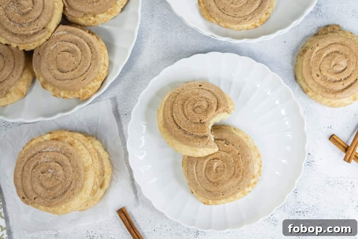 25 Office Cookies Everyone Brings and Raves About 8 Crumbl Copycat Churro Cookies are arranged on white plates and a napkin. One cookie on a plate has a bite taken out. Two cinnamon sticks are placed nearby on the white surface.