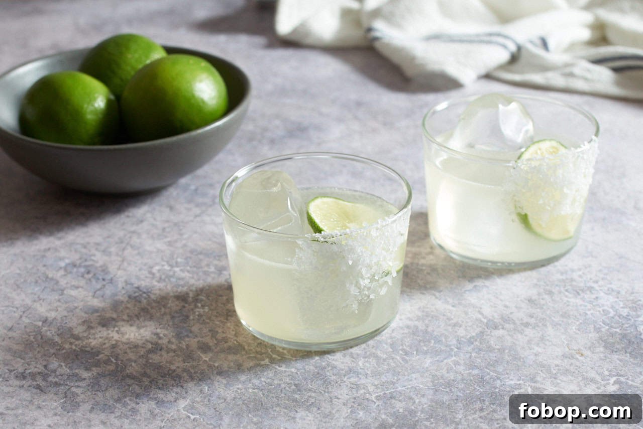 Smoky Mezcal Margarita Recipe: How to Make the Classic Cocktail 2 Two mezcal margaritas with salt, a bowl of limes and a blue and white striped towel are in the background.