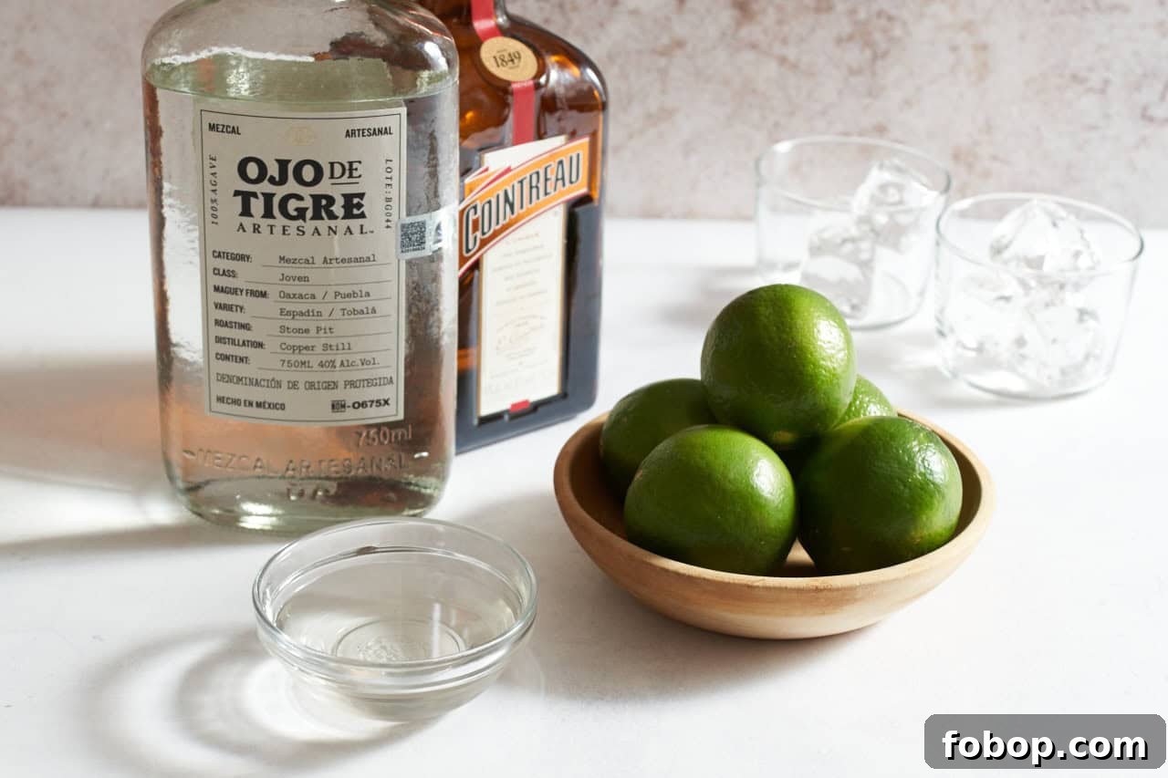 Smoky Mezcal Margarita Recipe: How to Make the Classic Cocktail 3 Bottles of mezcal and Cointreau next to a bowl of limes, a bowl of simple syrup, and two glasses filled with ice.