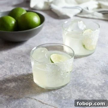 Smoky Mezcal Margarita Recipe: How to Make the Classic Cocktail 6 Two mezcal margaritas with salt, a bowl of limes and a blue and white striped towel are in the background.