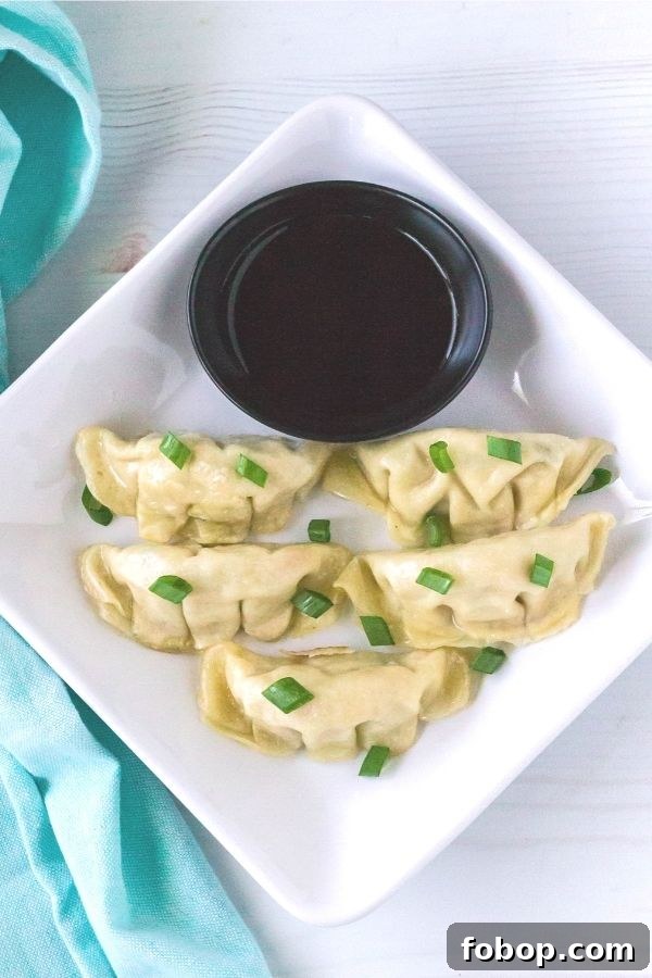 Instant Pot Frozen Dumplings (Potstickers) in Minutes 3 Square white plate with five Asian dumplings on it, topped with green onions, served with a small bowl of soy sauce for dipping.