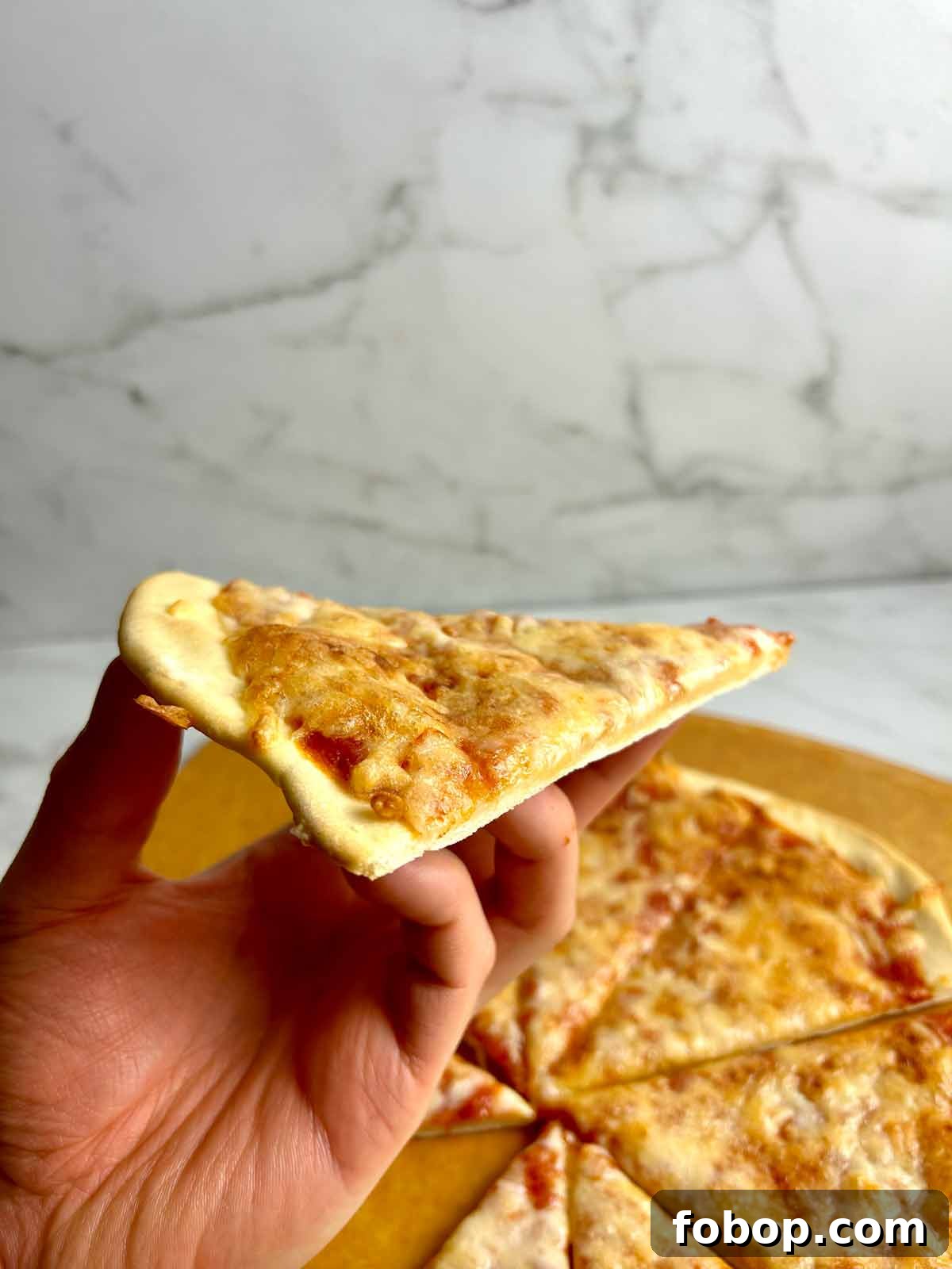 Crispy Cracker-Crust Pizza Recipe: Thin, Crunchy Homemade Pie 12 hand holding slice of cracker crust pizza
