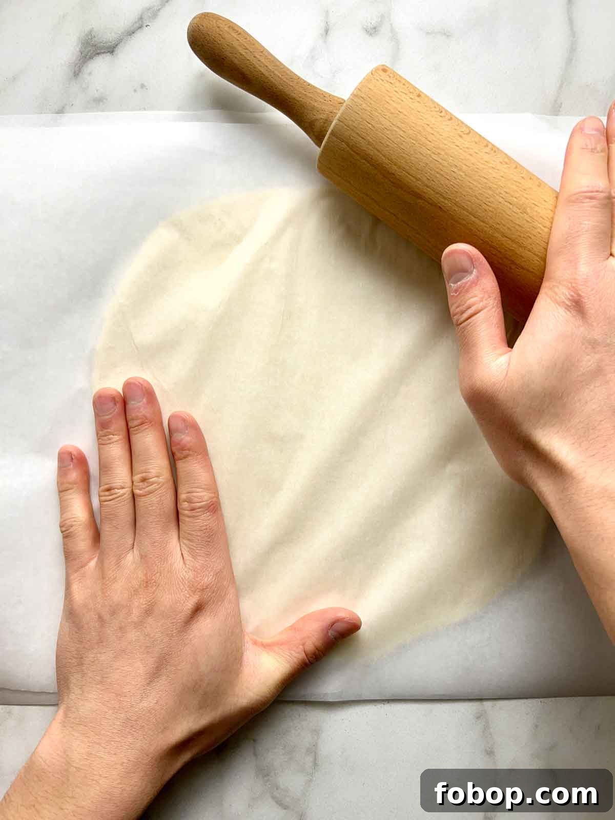 Crispy Cracker-Crust Pizza Recipe: Thin, Crunchy Homemade Pie 6 dough between two pieces of parchment paper being rolled out with a rolling pin