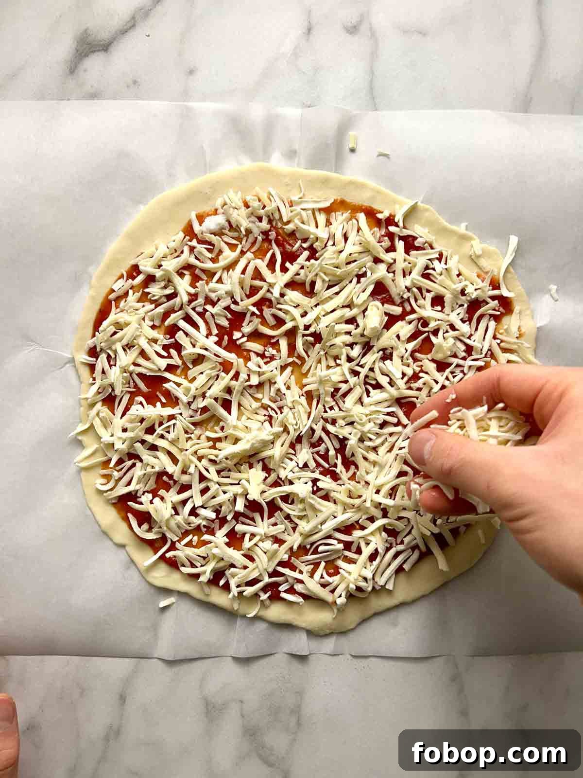 Crispy Cracker-Crust Pizza Recipe: Thin, Crunchy Homemade Pie 9 cheese being sprinkled onto pizza