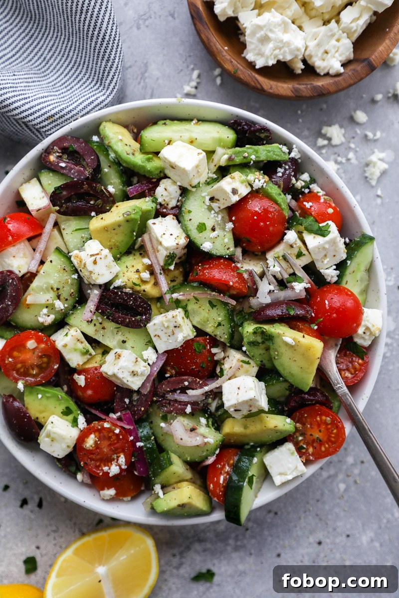 Greek salad made with sliced avocado, english cucumbers, tomatoes, red onion, kalamata olives and feta cheese tossed in a lemony Greek dressing
