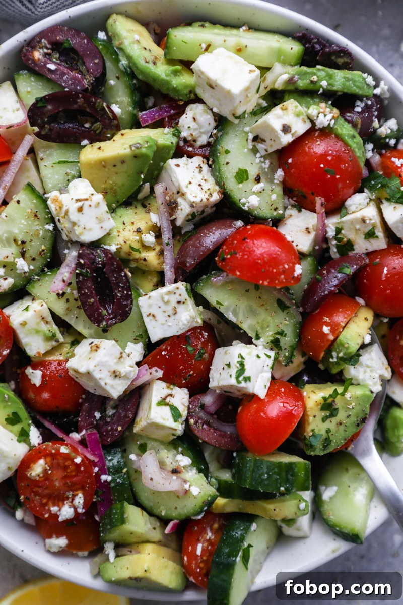 Avocado, cherry tomatoes, cucumber, red onion, Greek olives, feta cheese, salt and pepper tossed in a bowl drizzled with a red wine vinegar and lemon dressing