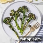 Roasted broccolini on a plate with lemon slices and a fork.