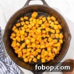Cubed butternut squash in a skillet on a marble countertop.