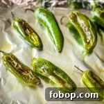 Roasted jalapenos on a foil-lined sheet tray.