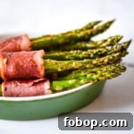 Side view of turkey bacon wrapped asparagus in a green dish.