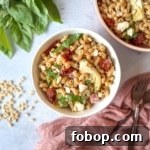 Whole wheat pasta salad in a white bowl surrounded by fresh basil.