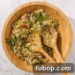 A wooden bowl filled with orzo pesto salad mixed with arugula, sun-dried tomatoes, feta cheese.