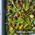 Roasted brussels sprouts and asparagus sit on a blue sheet tray.