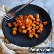 Cubed, sautéed sweet potatoes sit on a black plate with a gold fork.
