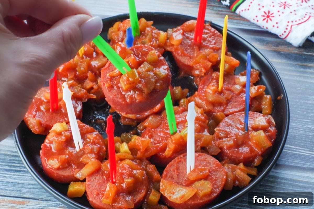 slow cooker kielbasa appetizer on a green plastic skewer being picked up