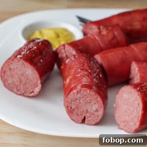several pieces of kielbasa on a white plate with a small white dish of mustard