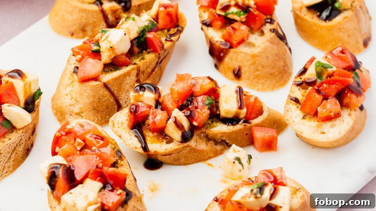 Several slices of gluten-free bruschetta with tomato, mozzarella and a balsamic glaze drizzle on a marble platter.