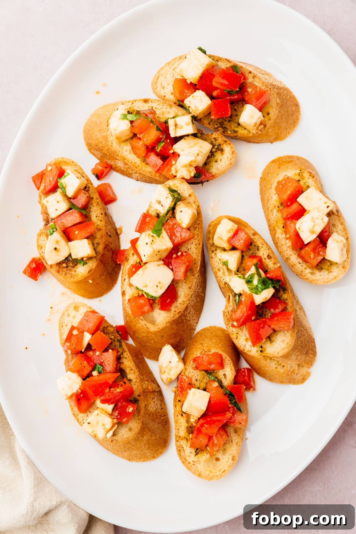 Eight pieces of gluten-free bread topped with diced tomatoes, diced mozzarella and basil on a white oval platter.