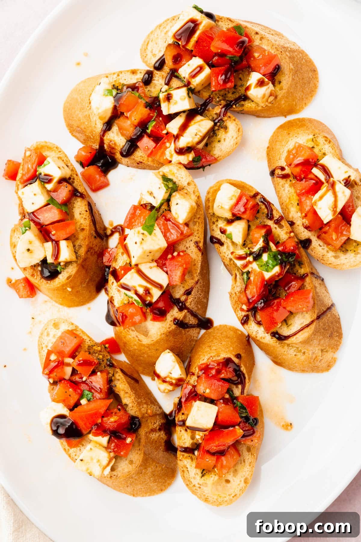 An overhead view of eight pieces of gluten free bruschetta with diced tomatoes, diced fresh mozzarella, basil and drizzle of balsamic glaze.