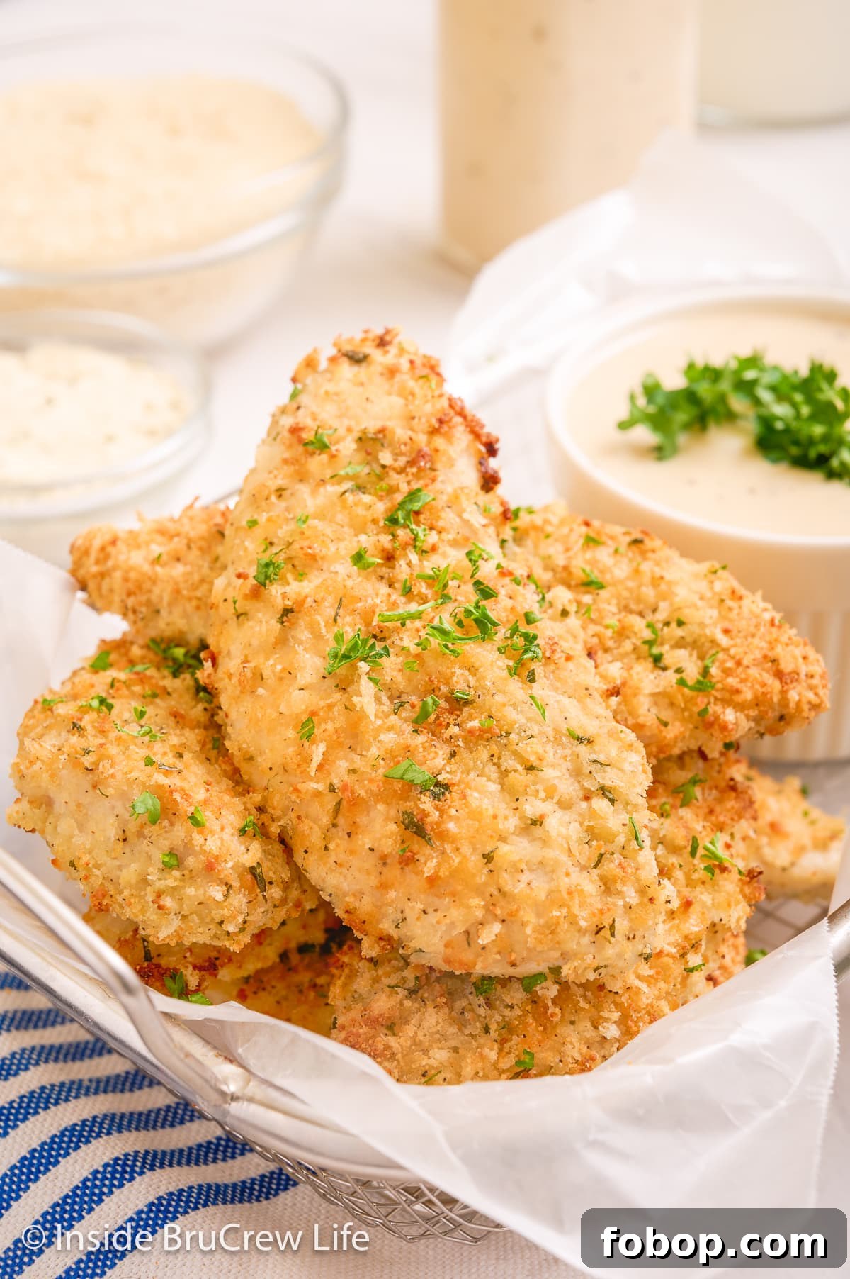 Crispy Parmesan Chicken Tenders with Garlic Herb Dipping Sauce 2 Breaded chicken strips in a wire basket.