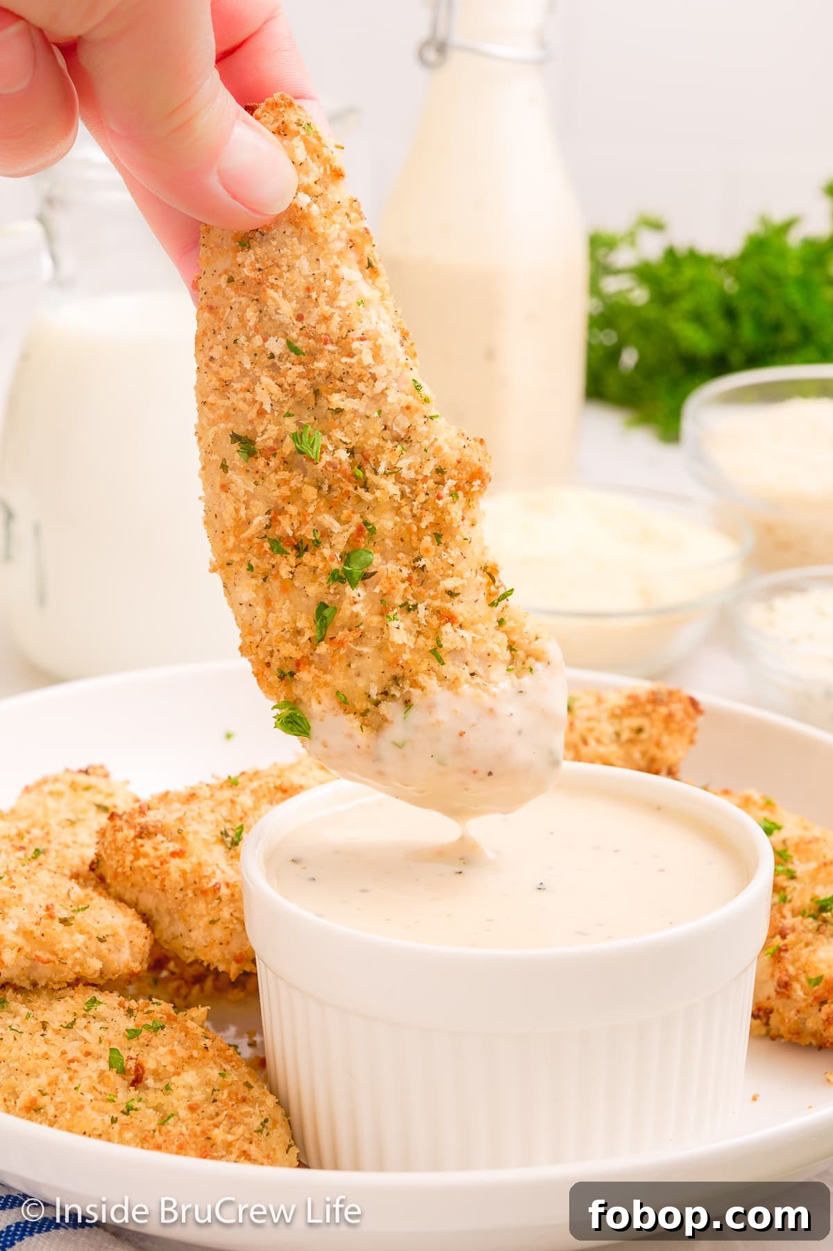 Crispy Parmesan Chicken Tenders with Garlic Herb Dipping Sauce 5 A crispy chicken tender being dipped in ranch dressing.