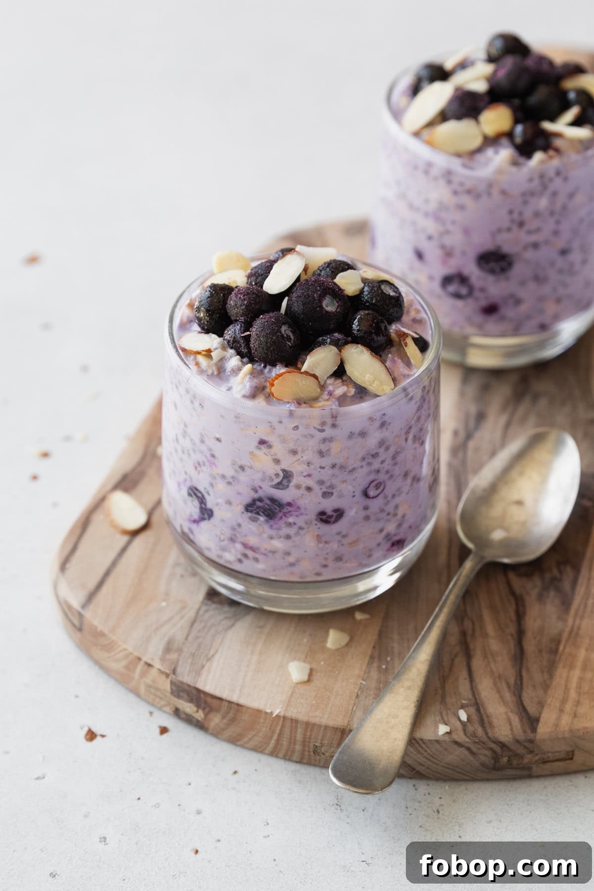 Creamy Blueberry Overnight Oats Recipe for Quick Breakfast 2 Two glass of blueberry overnight oats on a wooden board with a spoon.