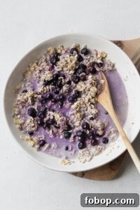 Creamy Blueberry Overnight Oats Recipe for Quick Breakfast 5 Blueberry overnight oats being mixed together in a white bowl with a wooden spoon.