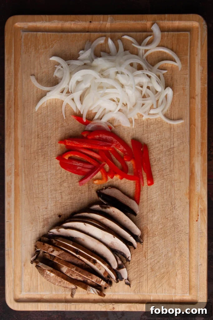 Sliced onions, red peppers, and portobello mushrooms on a cutting board. 
