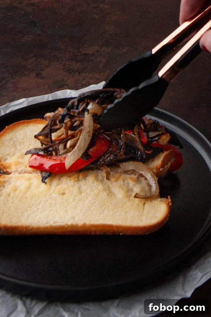 Adding roasted vegetables to a toasted hoagie before completing the vegetarian cheesesteak with cheese sauce.