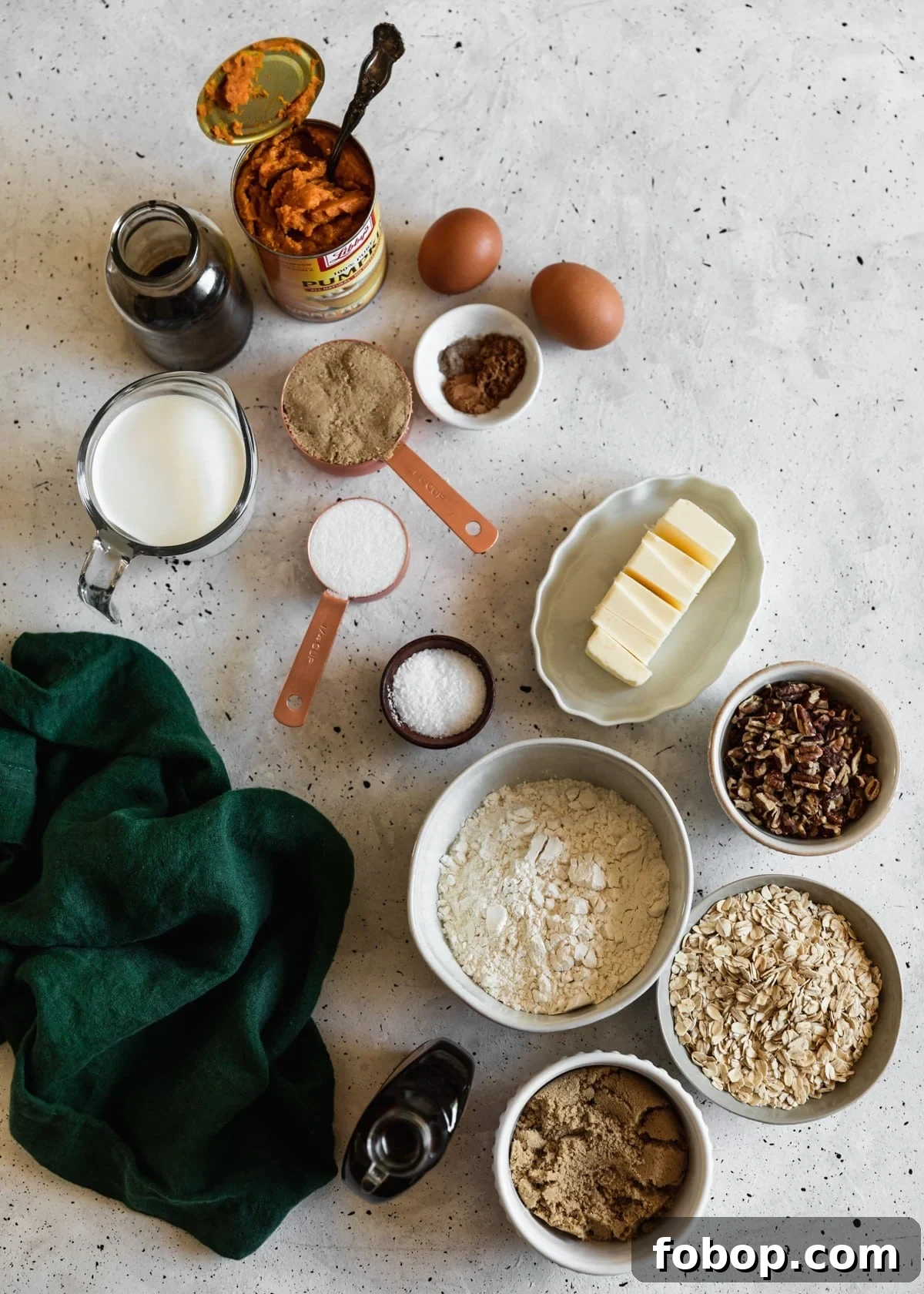 Maple Oat Streusel Pumpkin Crisp Recipe 3 An overhead of various white and grey bowls with baking ingredients like flour, oats, pecans, sugar, and butter on a white speckled counter next to a can of pumpkin and dark green linen.