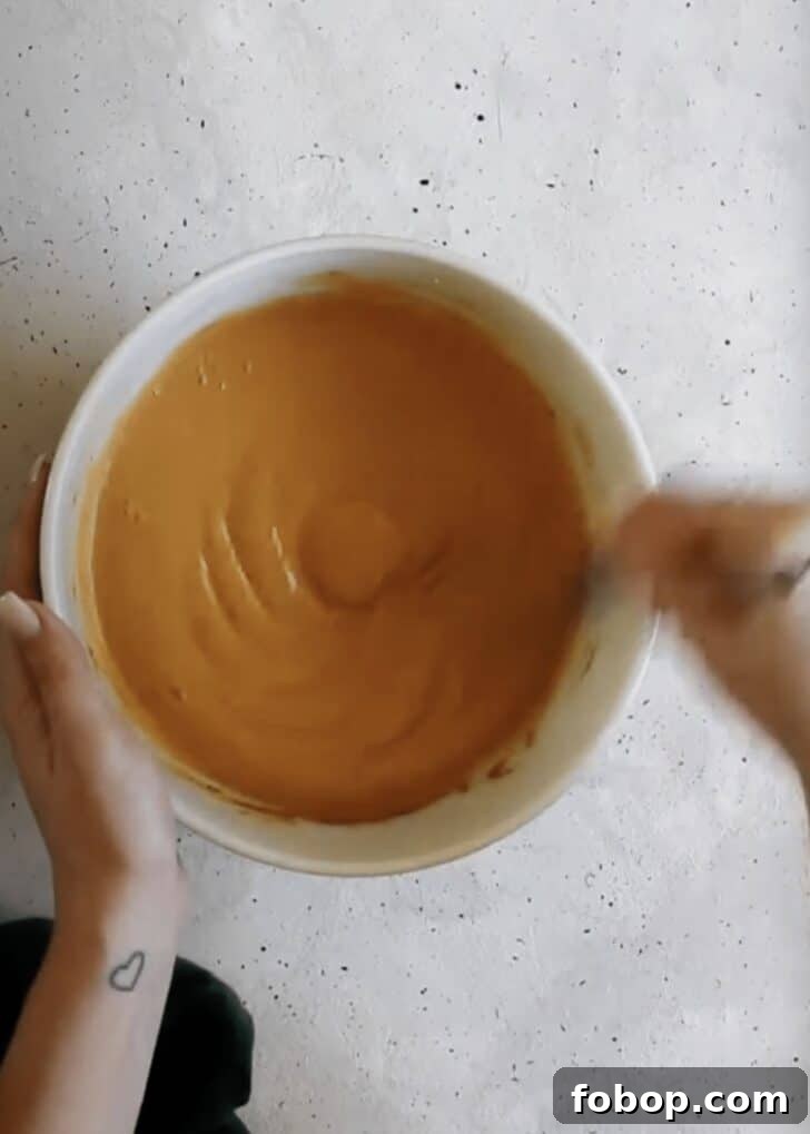 Maple Oat Streusel Pumpkin Crisp Recipe 4 A hand using a whisk to mix pumpkin filling in a white bowl on a grey counter.