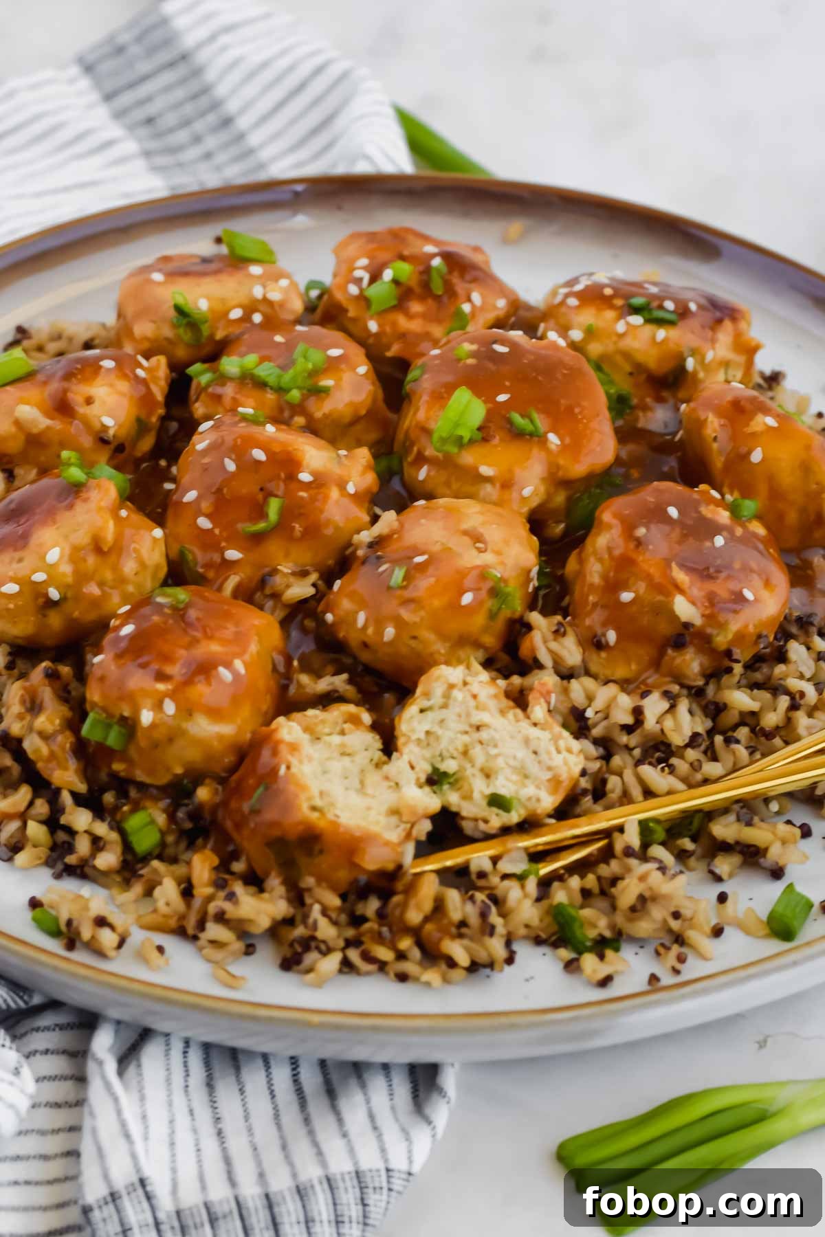 Sticky Asian Chicken Meatballs with Ginger Soy Glaze 2 Asian chicken meatballs over bed of rice on white plate with chopsticks.