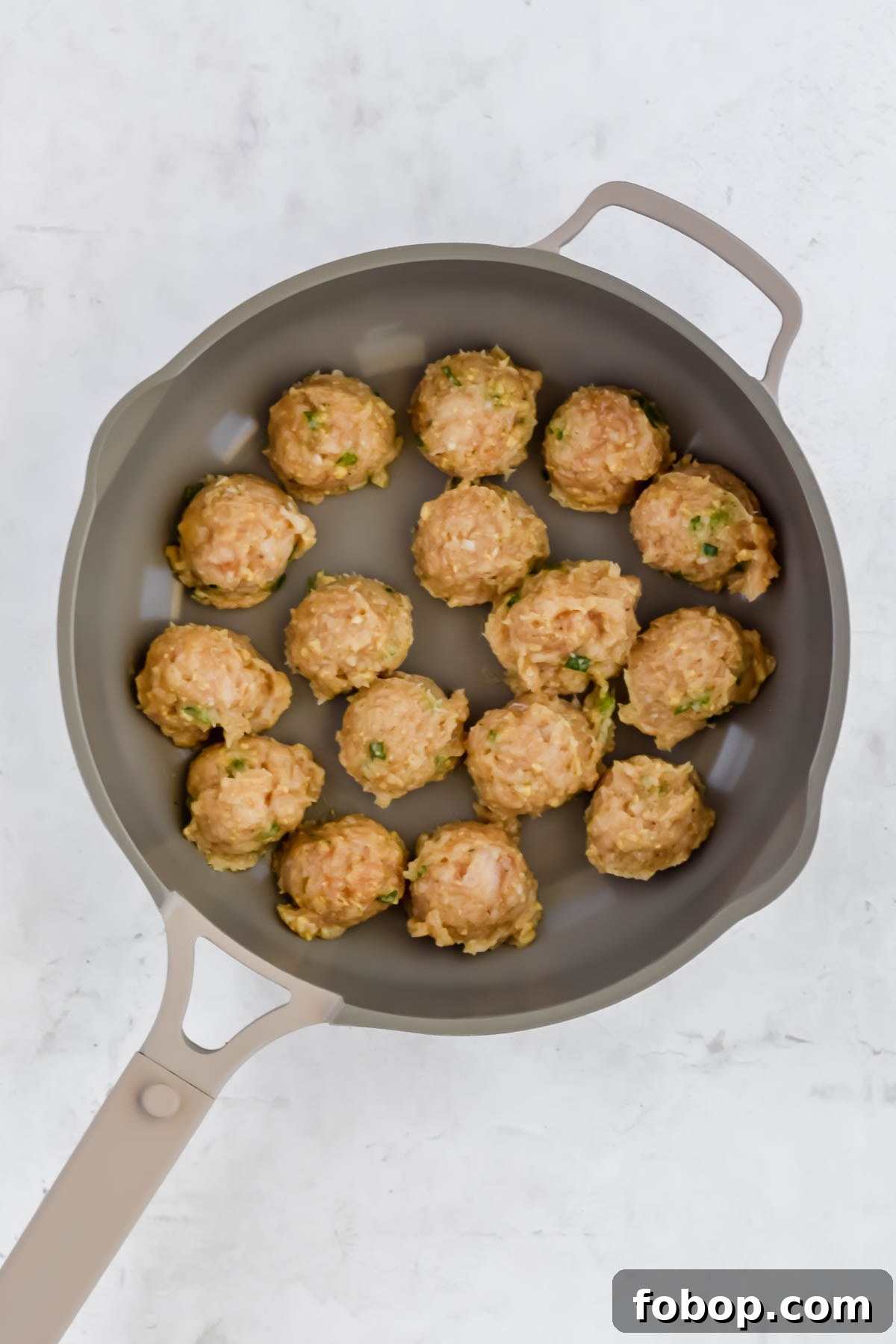 Sticky Asian Chicken Meatballs with Ginger Soy Glaze 6 formed raw Asian chicken meatballs in pan on white background.
