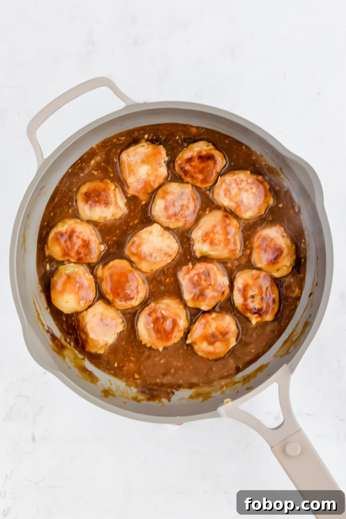 Sticky Asian Chicken Meatballs with Ginger Soy Glaze 7 formed raw Asian chicken meatballs with teriyaki sauce in pan on white background.