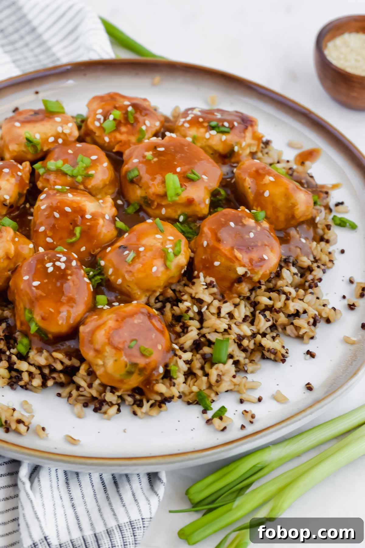 Sticky Asian Chicken Meatballs with Ginger Soy Glaze 8 Asian chicken meatballs over bed of rice on white plate and garnished with green onion.