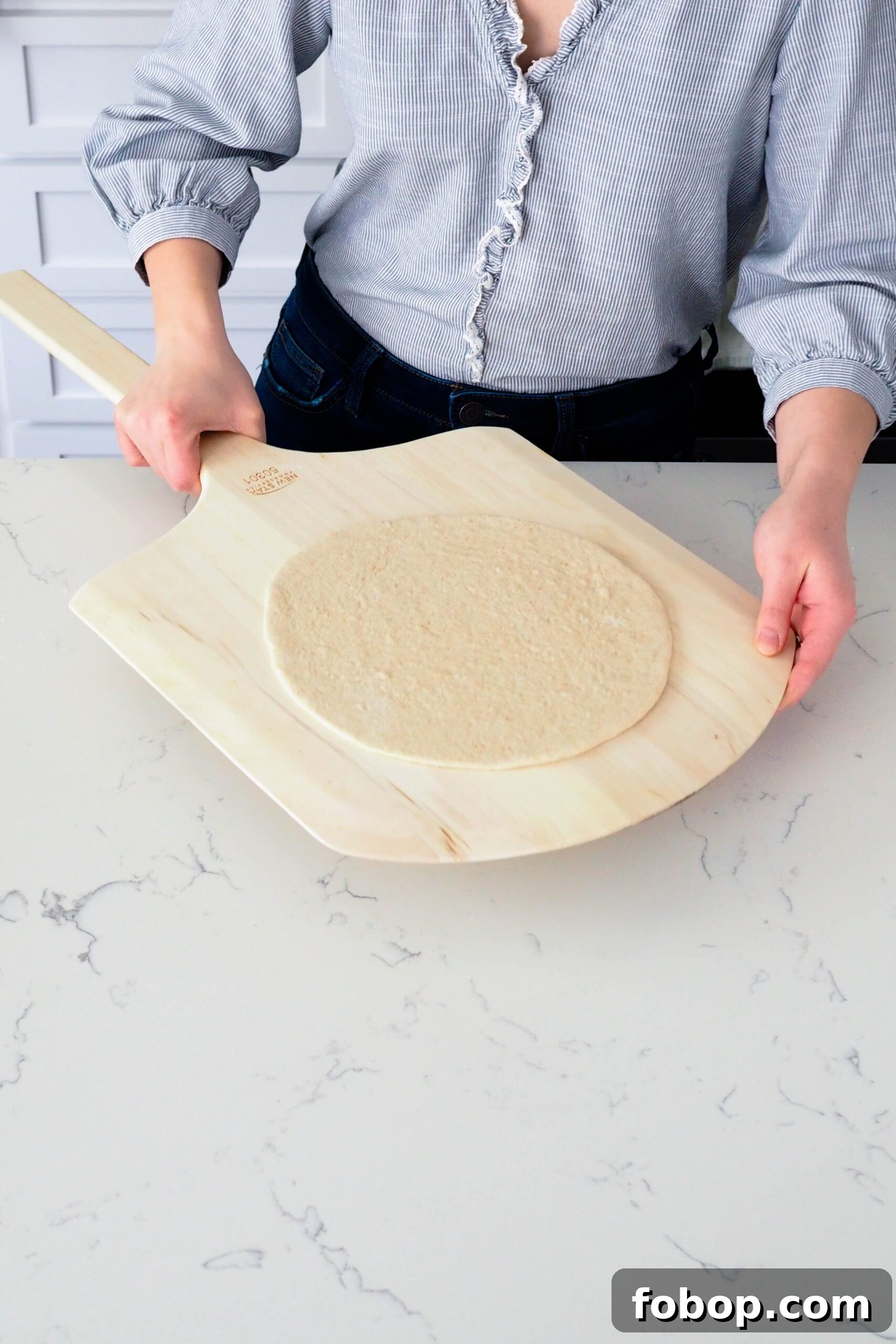 A rolled out crust is positioned on a pizza peel.