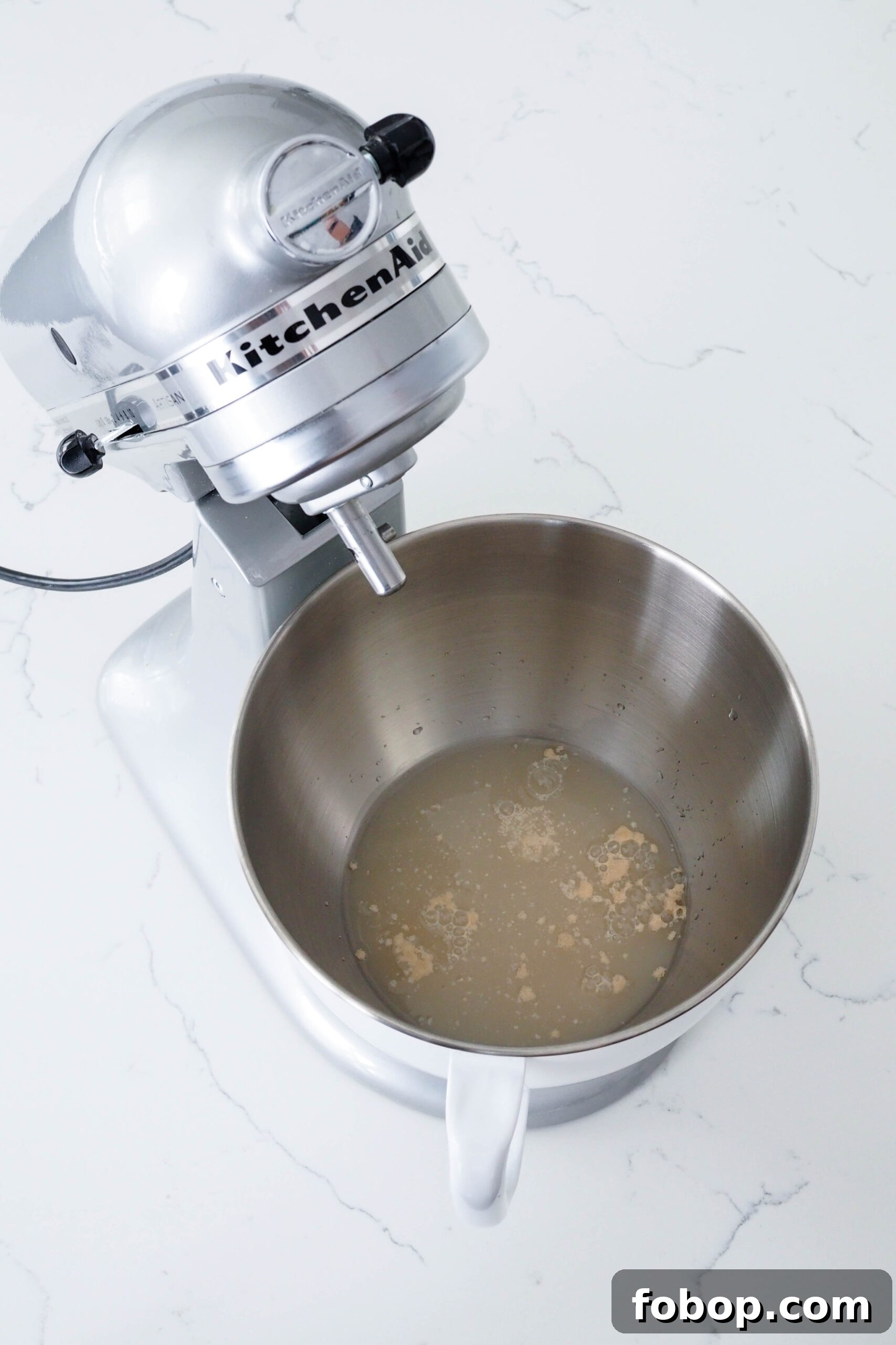 Yeast dissolves in water in a stand mixer bowl.