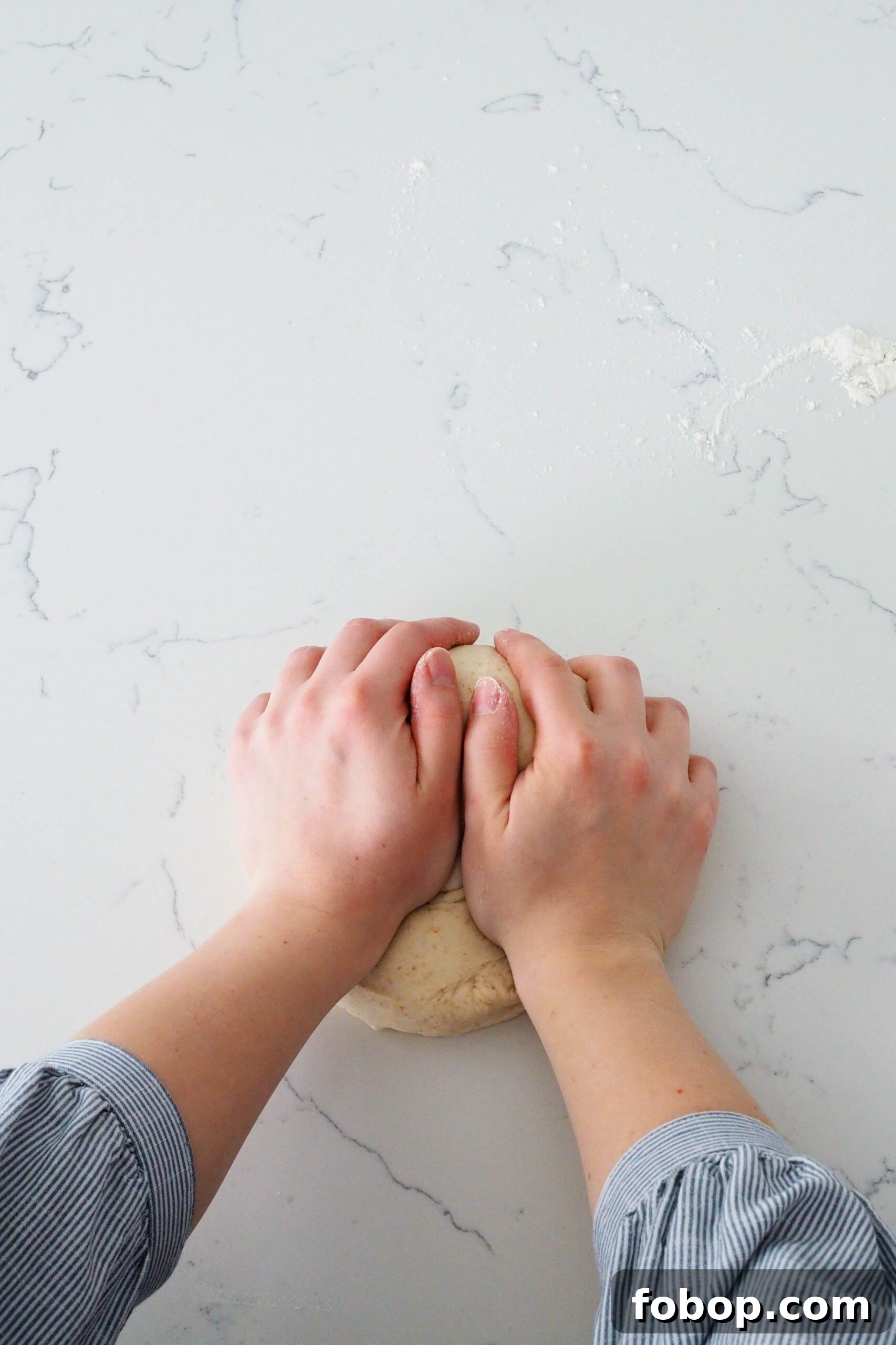 Two hands knead a ball of thin crust pizza dough.